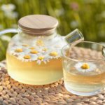 Close-up glass teapot with a mug of aromatic chamomile tea on nature background