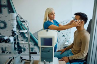 Happy ophthalmologist using testing eyeglasses during eye exam of her patient at the clinic.